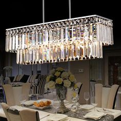 a chandelier hanging over a dining room table with white chairs and plates on it