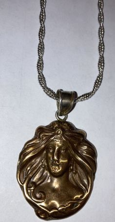 a gold pendant with a woman's face on it, hanging from a silver chain