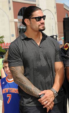 a man with tattoos on his arm walking in front of a group of people wearing sunglasses