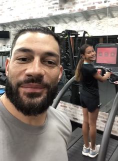 a man with a beard standing next to a woman on a treadmill in a gym