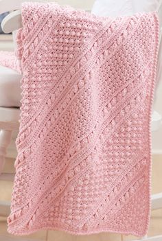 a pink knitted blanket sitting on top of a chair next to a white rocking chair
