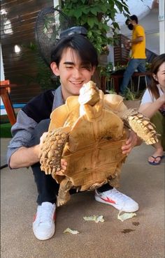 a young man is holding up a large tortoise shell