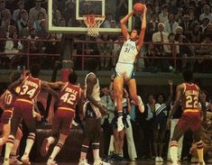 a group of men playing basketball against each other in front of an arena full of people