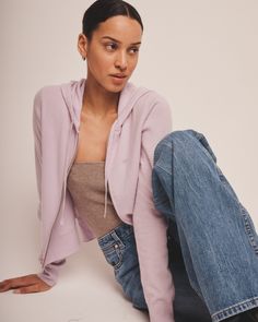 a woman is sitting on the ground wearing jeans and a pink sweater with a hoodie