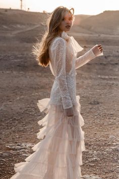 a woman standing in the desert wearing a dress with sheer sleeves and ruffles