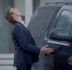 a man in a suit leaning on the door of a car with his eyes closed