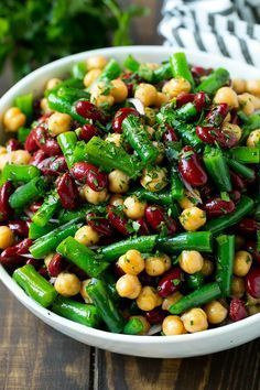 a white bowl filled with beans and green beans on top of a wooden table next to a
