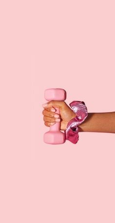 a woman's hand holding two pink dumbs against a pink background