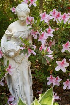 a statue is surrounded by pink flowers and green leaves