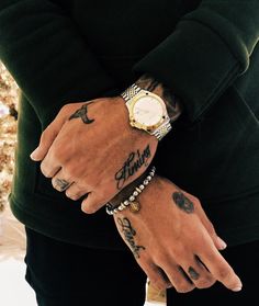 a man with tattoos on his arm and wrist wearing a watch, standing in front of a christmas tree