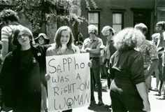 a group of people standing around each other holding a sign that says sappho was a right - on woman
