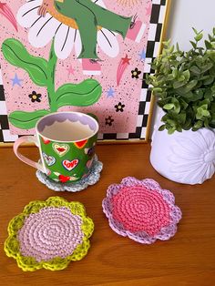 three crocheted coasters sitting on a table next to a potted plant