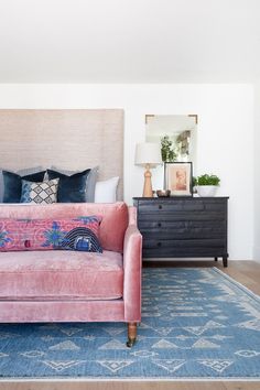 a pink couch sitting on top of a blue rug in a living room next to a dresser