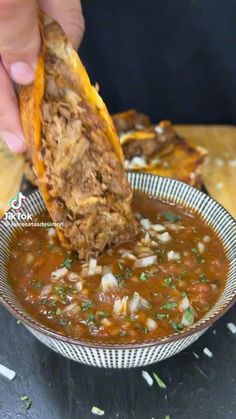 a person dipping some food into a bowl with tortilla chips on the side