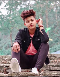 a young man sitting on the ground with his hands in his ears and looking at the camera