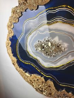 a blue and gold plate with some silver rocks in it's center, on a white surface