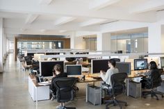 two people sitting at desks in an office with multiple monitors and laptops on them