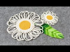 two crocheted flowers with green leaves sitting on top of a gray tablecloth