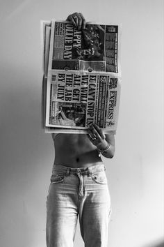 a man with no shirt is holding up a bunch of newspapers in front of his face