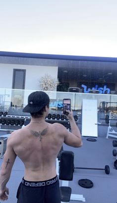 a man with no shirt is taking a selfie in the gym while holding his cell phone