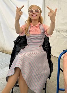 a woman sitting on top of a chair with her hands in the air while wearing glasses