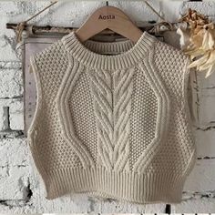 a white sweater hanging on a brick wall next to a wooden hanger with dried flowers