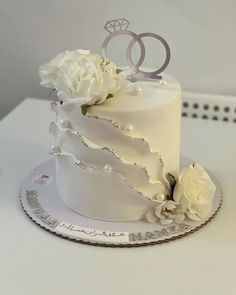 a wedding cake with white flowers and two rings on top