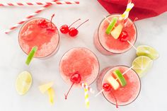 three glasses filled with fruit and garnish on top of a table