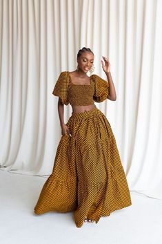 a woman standing in front of a white curtain wearing a brown and yellow patterned dress