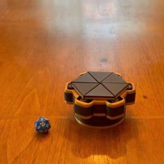 a wooden table topped with a black and brown box next to a blue dice on top of it