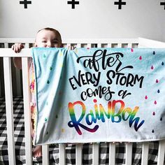 a baby in a crib holding up a blanket that says after every storm comes a rainbow