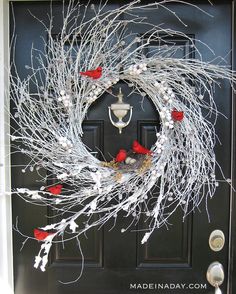 a wreath with white branches and red birds hanging from it's center, in front of a black door