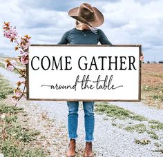 a woman holding a sign that says, come gather around the table