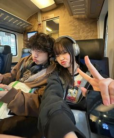 two people sitting on a train with their hands in the air and pointing at something