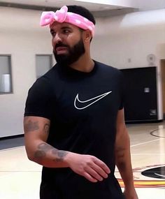 a man with a pink bow on his head is standing in an indoor basketball court