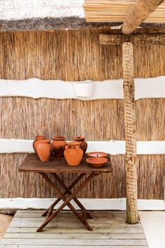 a table with vases on it in front of a straw hut