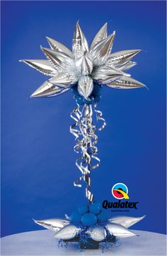 a silver star decoration on top of a table with blue balls and streamers hanging from it