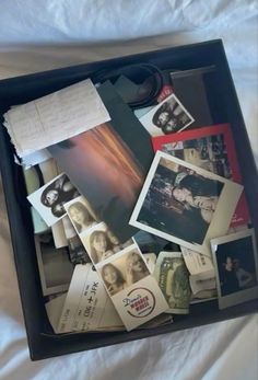 an open suitcase filled with photos and papers on top of a white sheet covered bed