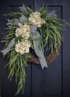 a wreath with white flowers and greenery hanging on a black front door, decorated with ribbon