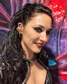 a woman with long black hair and piercings on her ears smiles at the camera