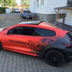 an orange sports car parked in front of a building on the side of a street