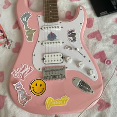 a pink guitar with stickers on it sitting on a bed next to a laptop