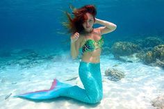 a woman with red hair is sitting on the bottom of a mermaid tail under water