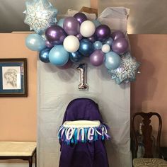 a purple chair sitting under a bunch of balloons on top of a wooden table next to a wall