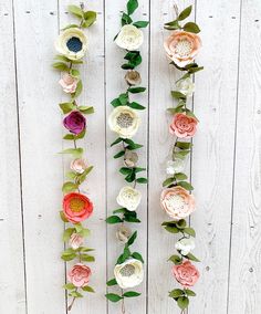 flowers are arranged on the side of a white wall with green leaves and stems attached to them