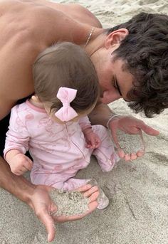 a man kissing a baby on the beach with sand all around him and her feet in the sand