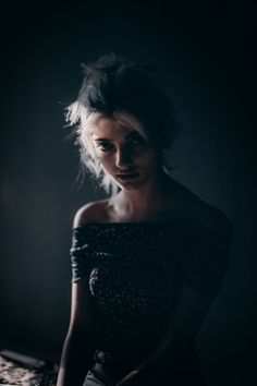 a woman sitting on top of a bed in a dark room with her hair blowing