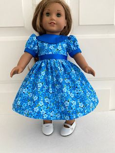 an american girl doll wearing a blue dress and white shoes, standing in front of a door