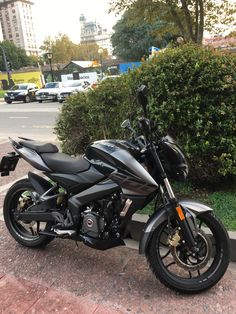 a black motorcycle parked on the side of a road next to a bush and bushes