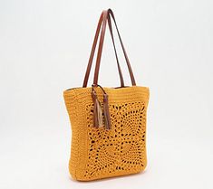 an orange crocheted bag with brown handles and straps on the handle, sitting against a white background